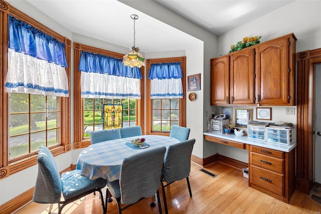 dining area with light wood-style floors, visible vents, baseboards, and built in desk