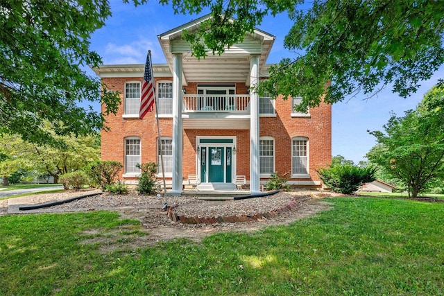 greek revival house with brick siding, a balcony, and a front lawn