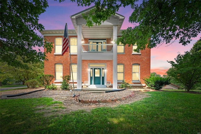 back house at dusk with a balcony and a yard