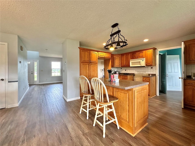 kitchen featuring a breakfast bar, tasteful backsplash, dark hardwood / wood-style flooring, hanging light fixtures, and a center island