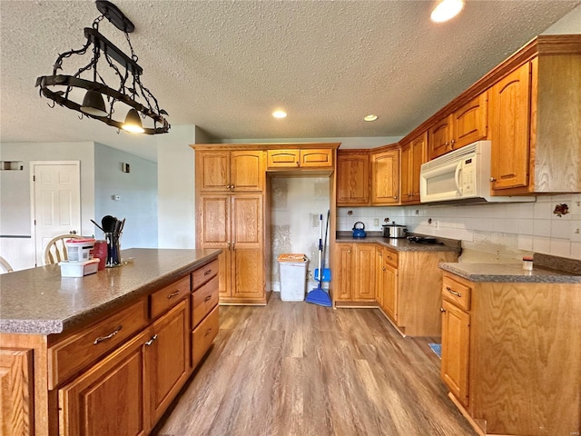 kitchen featuring tasteful backsplash, decorative light fixtures, a center island, a textured ceiling, and light hardwood / wood-style floors