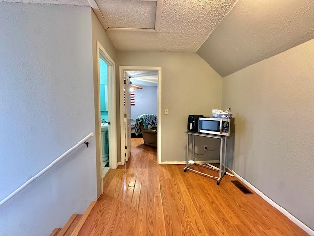 corridor featuring lofted ceiling, a textured ceiling, and light hardwood / wood-style flooring