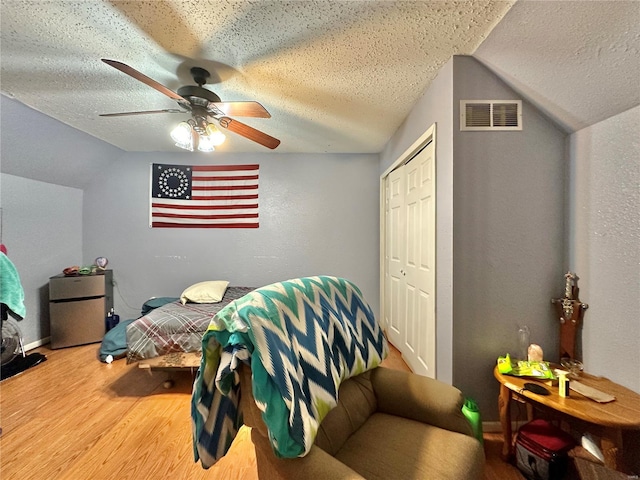 bedroom featuring hardwood / wood-style flooring, vaulted ceiling, stainless steel refrigerator, and a textured ceiling