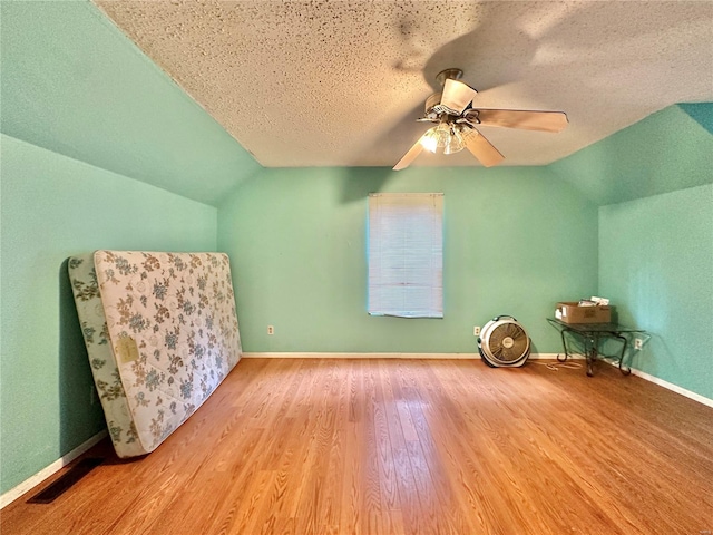 additional living space featuring hardwood / wood-style flooring, ceiling fan, vaulted ceiling, and a textured ceiling