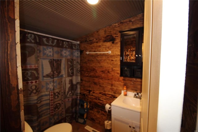 bathroom featuring vanity, wood walls, curtained shower, toilet, and lofted ceiling