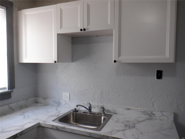 kitchen with sink, white cabinetry, light stone countertops, and plenty of natural light