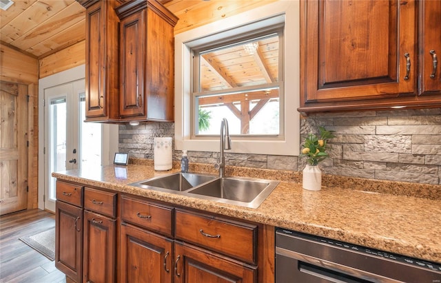kitchen featuring brown cabinets, dishwasher, wood finished floors, a sink, and decorative backsplash
