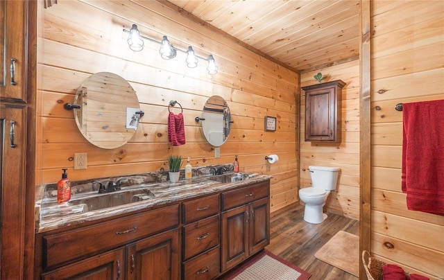 bathroom with a sink, double vanity, toilet, wood finished floors, and wooden walls