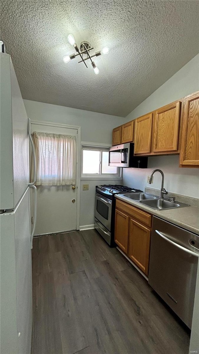 kitchen featuring sink, dark wood-type flooring, stainless steel appliances, a textured ceiling, and vaulted ceiling