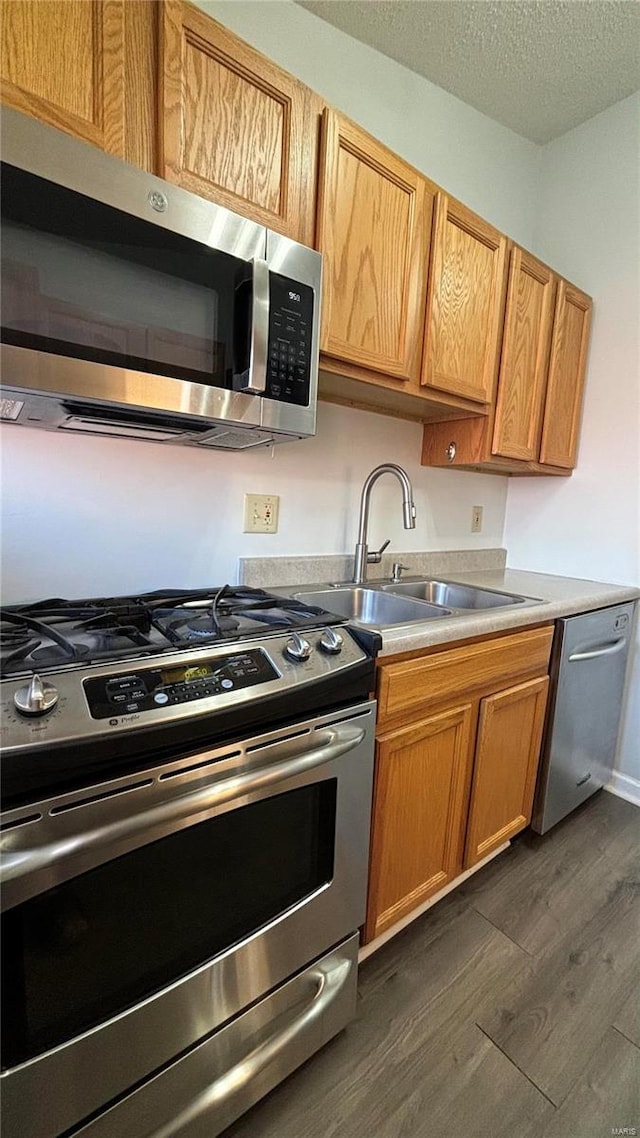 kitchen with appliances with stainless steel finishes, sink, a textured ceiling, and dark hardwood / wood-style floors