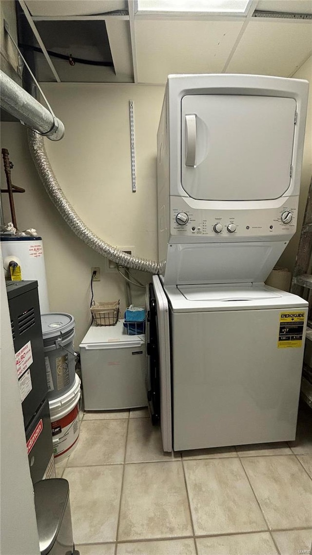 laundry area featuring stacked washer / drying machine, water heater, and light tile patterned floors