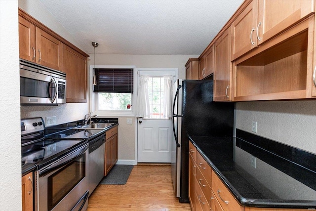 kitchen featuring dark stone counters, sink, light wood-type flooring, a textured ceiling, and stainless steel appliances