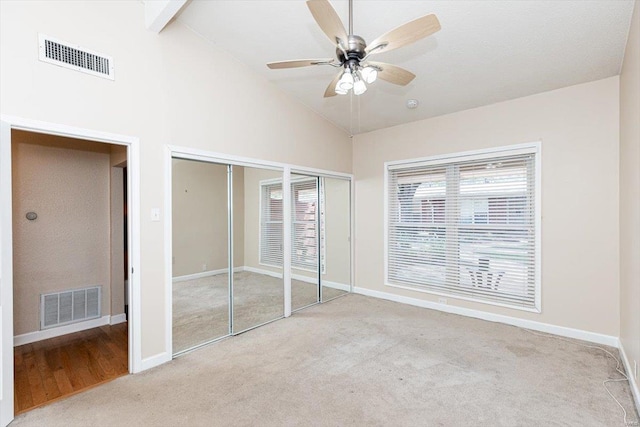 unfurnished bedroom featuring ceiling fan, carpet flooring, multiple closets, and high vaulted ceiling