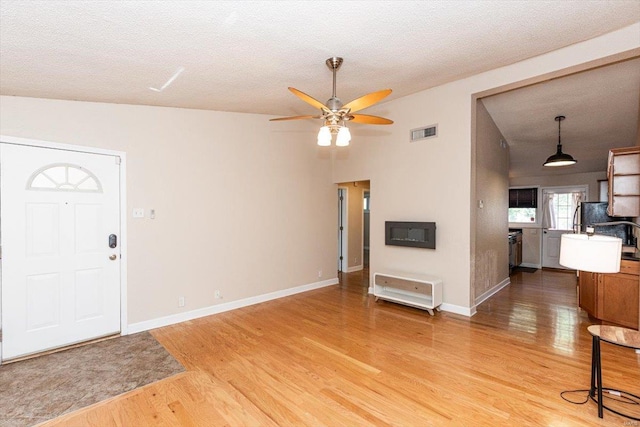 unfurnished living room with ceiling fan, lofted ceiling, a textured ceiling, and hardwood / wood-style flooring