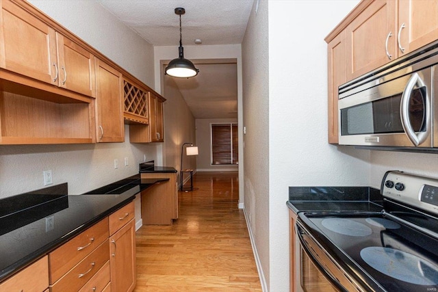 kitchen featuring appliances with stainless steel finishes, light hardwood / wood-style flooring, a textured ceiling, dark stone counters, and hanging light fixtures