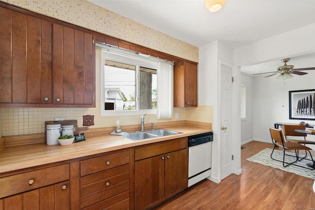 kitchen with a sink, dishwasher, baseboards, decorative backsplash, and wood finished floors