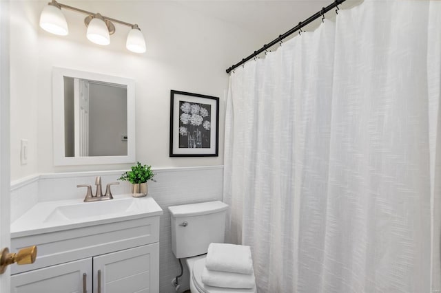 full bath featuring vanity, toilet, tile walls, and a wainscoted wall