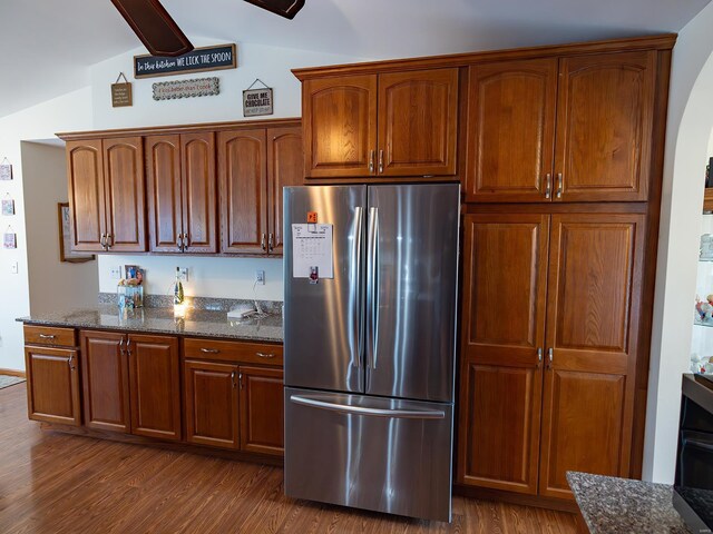 kitchen with vaulted ceiling, dark wood-type flooring, dark stone counters, and stainless steel fridge