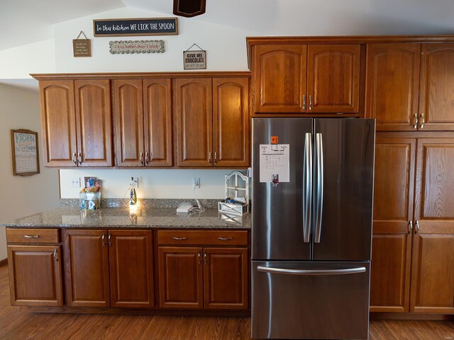 kitchen featuring dark stone counters, stainless steel refrigerator, wood-type flooring, and lofted ceiling