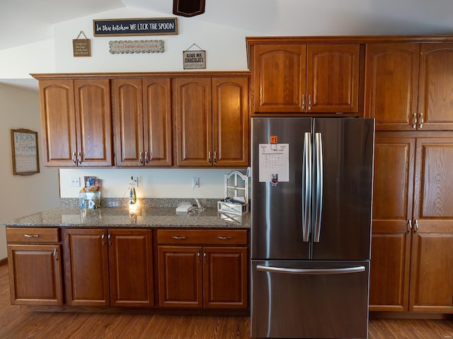 kitchen with dark wood-style flooring, vaulted ceiling, freestanding refrigerator, brown cabinetry, and dark stone countertops