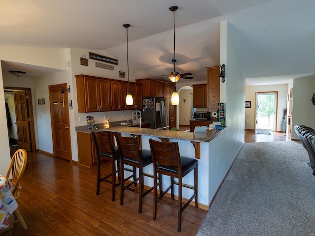 kitchen with arched walkways, stainless steel appliances, stone countertops, dark wood-type flooring, and a peninsula