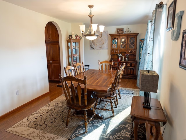 dining space featuring a chandelier, arched walkways, dark wood-style flooring, and baseboards