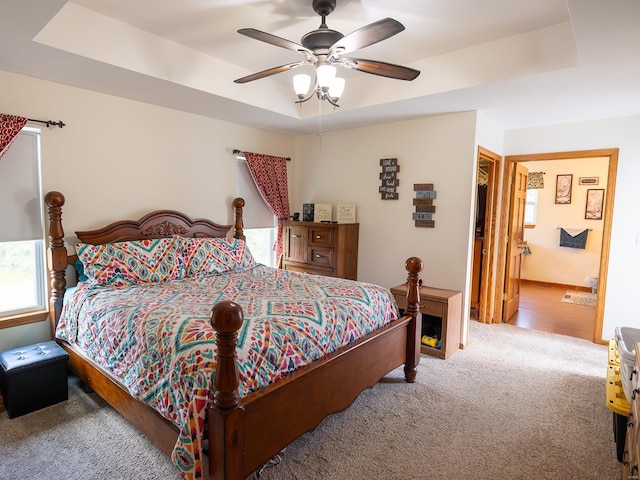 carpeted bedroom featuring connected bathroom, a raised ceiling, and a ceiling fan