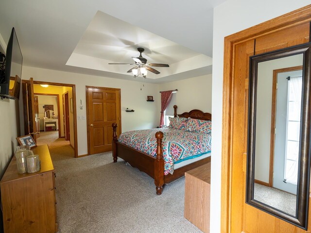 carpeted bedroom featuring ceiling fan, multiple windows, and a tray ceiling