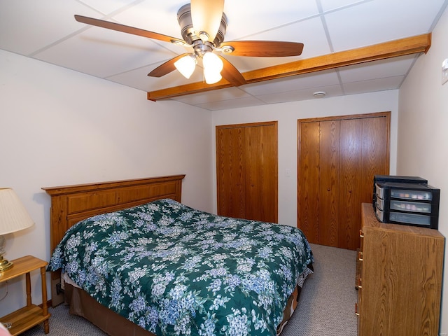 carpeted bedroom featuring a paneled ceiling, ceiling fan, and two closets