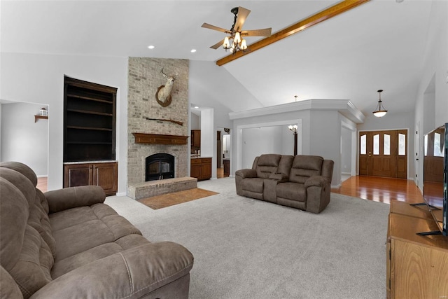 carpeted living room with high vaulted ceiling, beamed ceiling, ceiling fan, a brick fireplace, and built in shelves