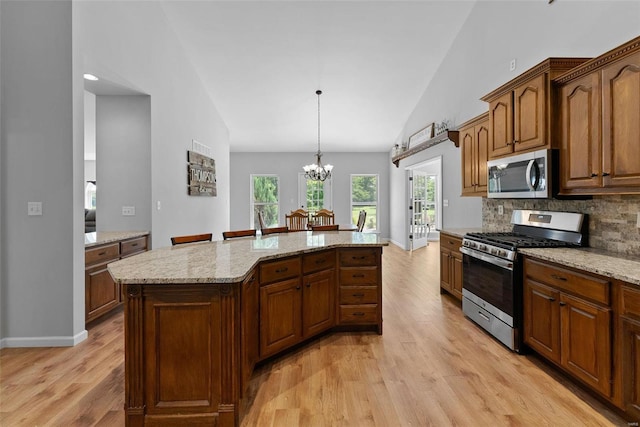 kitchen with appliances with stainless steel finishes, a center island, light hardwood / wood-style floors, and decorative light fixtures