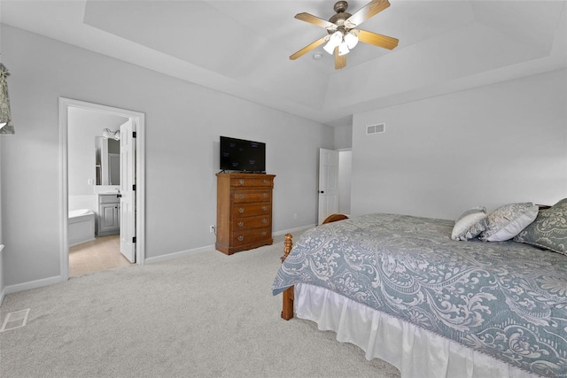 carpeted bedroom featuring a raised ceiling, connected bathroom, and ceiling fan