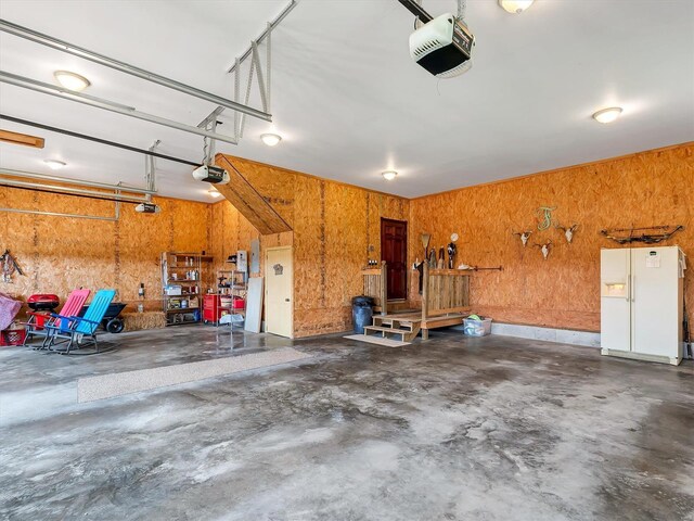 garage featuring a garage door opener, white refrigerator with ice dispenser, and wooden walls