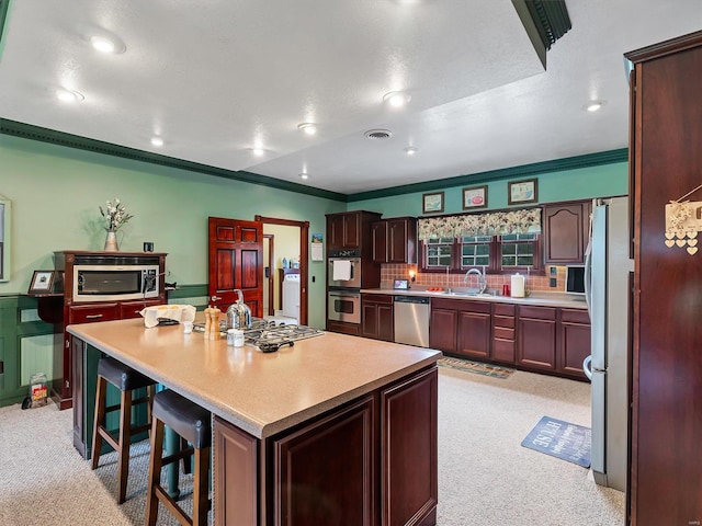 kitchen featuring appliances with stainless steel finishes, sink, a breakfast bar area, a center island, and crown molding