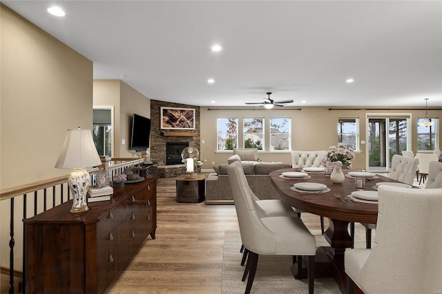 dining space featuring a stone fireplace, ceiling fan, and light hardwood / wood-style floors