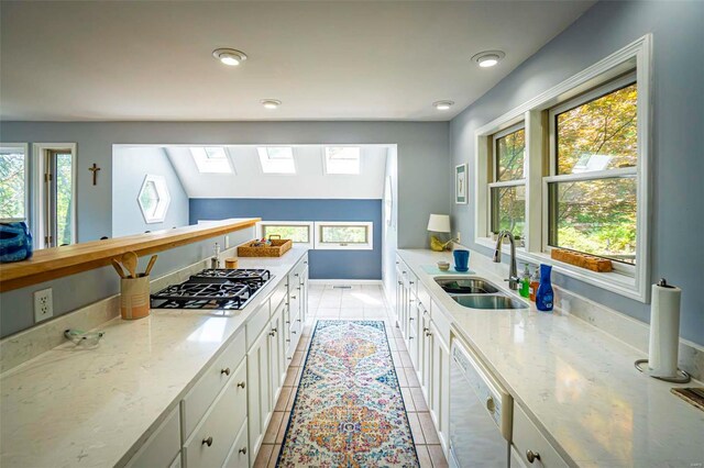 kitchen featuring a skylight, stainless steel gas stovetop, white dishwasher, white cabinetry, and light tile patterned flooring