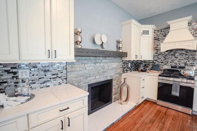 kitchen featuring tasteful backsplash, white cabinetry, custom exhaust hood, stainless steel gas range oven, and light hardwood / wood-style flooring