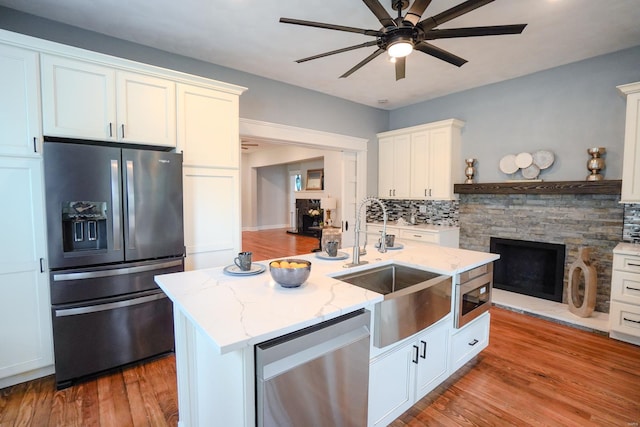 kitchen featuring sink, a kitchen island with sink, white cabinetry, stainless steel appliances, and a stone fireplace