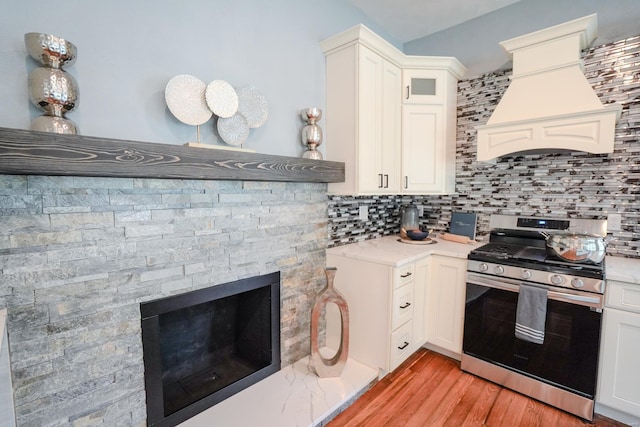 kitchen with stainless steel range with gas cooktop, backsplash, white cabinets, custom exhaust hood, and light hardwood / wood-style floors