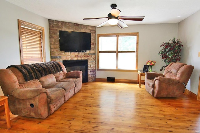 living room with a stone fireplace, ceiling fan, and light hardwood / wood-style flooring