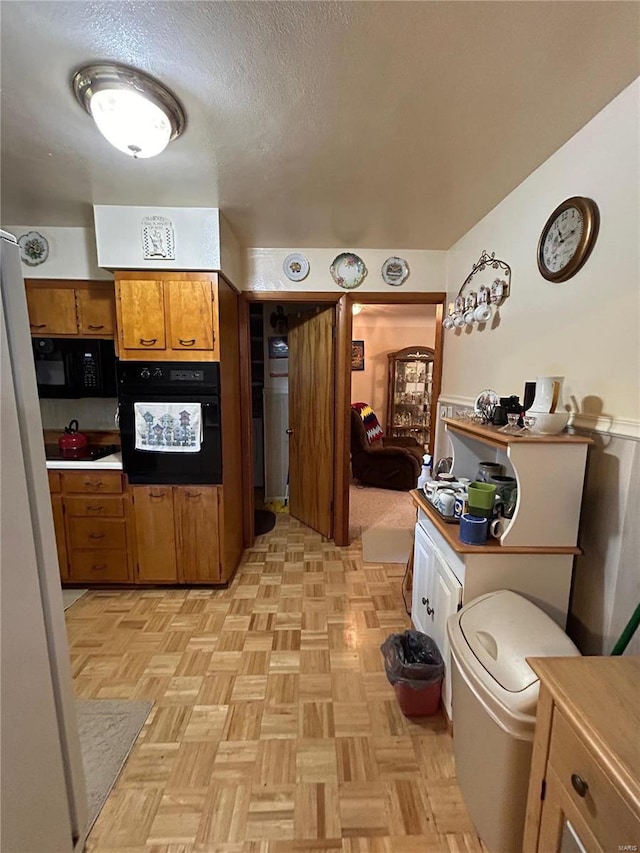 kitchen featuring a textured ceiling, black appliances, and light parquet floors