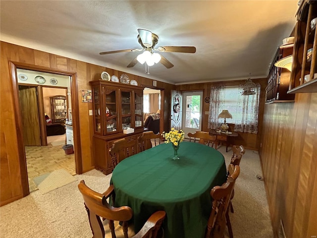 carpeted dining room with ceiling fan and wooden walls