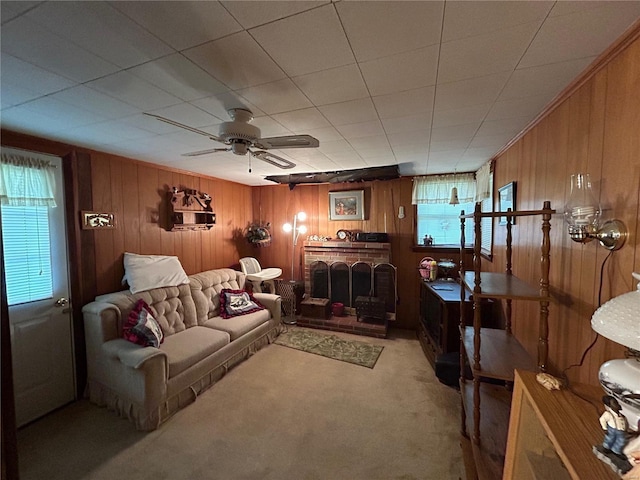 carpeted living room with ceiling fan, wooden walls, and a brick fireplace