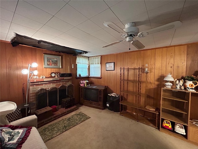 carpeted living room featuring a brick fireplace, wooden walls, and ceiling fan