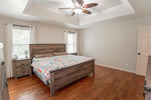 bedroom featuring ceiling fan, multiple windows, a tray ceiling, and hardwood / wood-style flooring