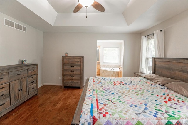 bedroom with a raised ceiling, dark hardwood / wood-style flooring, ensuite bath, and ceiling fan