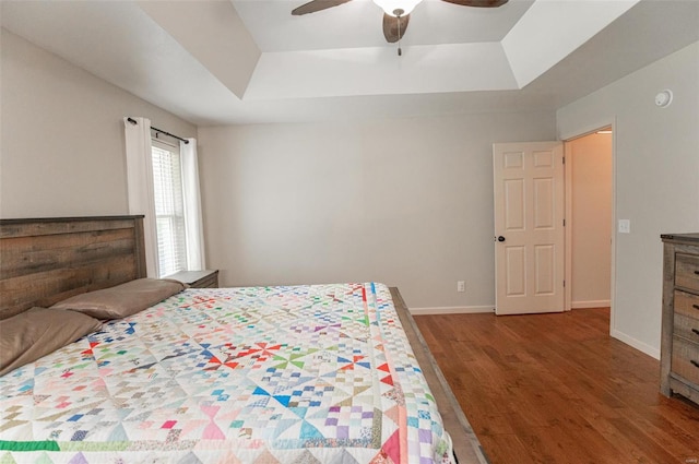 bedroom with hardwood / wood-style flooring, a raised ceiling, and ceiling fan