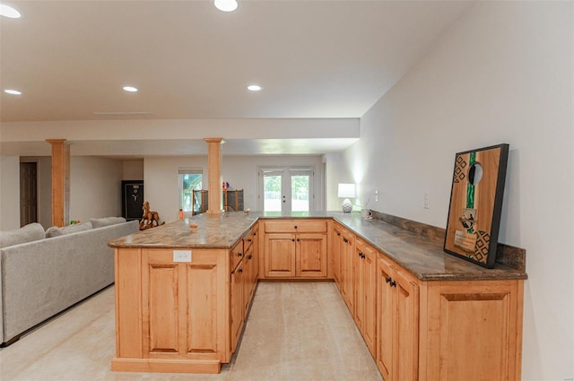 kitchen with light brown cabinets, decorative columns, kitchen peninsula, dark stone counters, and light colored carpet