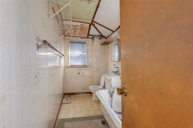 bathroom featuring a tub, toilet, vaulted ceiling, tile walls, and a sink