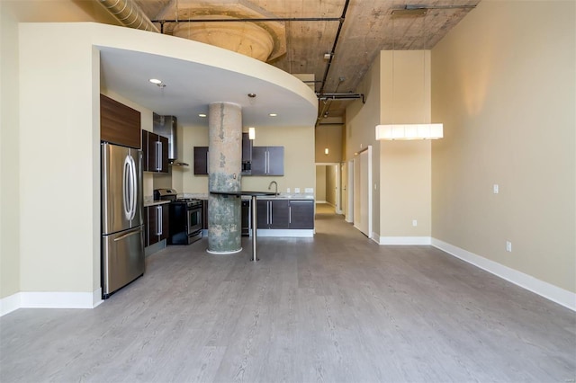 kitchen featuring dark brown cabinetry, a towering ceiling, a center island, and appliances with stainless steel finishes